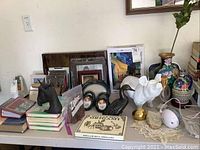 Lot with frames, statues, vases including black duck figure, white pig statue, brass bird, and photo albums on table