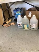 Boxed Arctic Air Pure Chill Max air purifier and cooler, electric blow dryer heater fan, shoe stretchers, and vinegar jugs on floor under table.