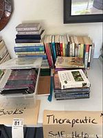 Photo of stacked books and a plastic container with blank CDs on a table, including various therapeutic and self-help books