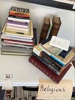 Two stacks of faith-based books on a table; including Bibles, religious texts, and inspirational titles with some old leather bound books.