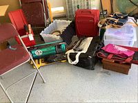 Photo showing an assortment of folding chairs, luggage, and storage containers arranged together with some bags and boxes on the ground.