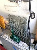 Two stacked metal grid storage racks leaned against wall, with mounting hardware nearby.