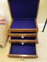 Top view of open silverware cabinet showing three drawers lined with blue fabric, with two drawers partially open revealing compartments and slots for organizing silverware.