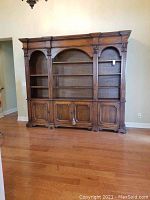 Full front view of assembled bookcase wall unit showing carved columns, arched shelves, and bottom cabinets