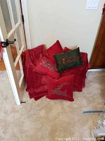 Red holiday pillows piled on floor with a red blanket, featuring sequined and embroidered holiday designs including reindeer.