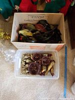 Box containing fragile glass bird figurines in assorted colors and a plastic container with gold and burgundy glittery ornaments and pine cones.
