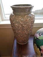 Tall vase with beige raised floral patterns on neutral background, placed by window