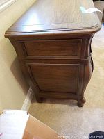 Side profile view showing the curved bombe shape, ornate panel carvings, and solid oak construction.
