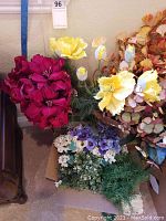 Silk flower arrangements featuring deep burgundy flowers, large yellow and white flowers, and clusters of purple, white, and green small flowers and foliage.