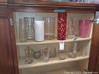 Glass cabinet shelf with 15 assorted vases, clear, white, red polka dot, and pink embossed floral designs
