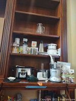 Shelf with Crock Pot slow roaster, Veggie Bullet food processor with accessories, coconut grater, citrus juicer, and recipe book.