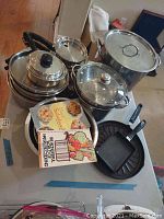 Overhead view of stacked stainless steel pots, pans and lids with two booklets on top