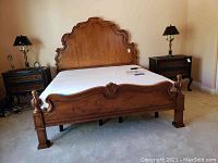 Full view of wood bed frame with mattress on, flanked by two dark wood nightstands with lamps and clock.