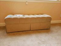Side view of beige tufted bench against a wall on carpet