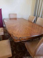 Full view of the polished wood dining table surrounded by upholstered chairs, showing its size and finish.