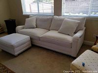 Full view of the linen sofa with two loose back pillows and matching ottoman next to it.