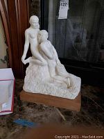 Full side view of Rodin reproduction statue showing both figures on textured base with wood base below.