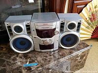 Full view of the Panasonic stereo system showing the central unit flanked by two speakers on a marble surface with a decorative fan in background.