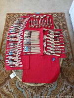Overview photo showing all pieces of the silverware set laid out on red cloth, separated by type of utensil.