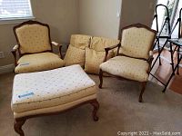 Pair of beige upholstered custom Calico Corners side chairs with wooden carved frames, matching ottoman, and some throw pillows lying behind chairs