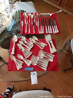 Full view of the silverware laid out on red cloth and table surface showing the quantity and variety of forks, knives, and spoons.