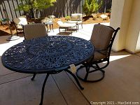 Metal outdoor round table with ornate scrollwork and built-in lazy Susan, surrounded by two swivel chairs with cushions.