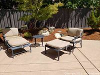 Full view of two armchairs with ottomans, small round table, and chaise lounge.