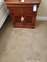 Front view of one wooden nightstand showing drawer with decorative tassel and double cabinet doors.