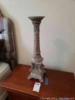 Front angle image of a single ornate votive candlestick showing tripod base and carved details.