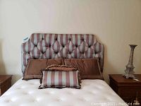 Front view of tufted striped fabric headboard, brown and striped decorative pillows, white mattress on bed frame