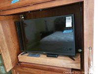 Front view of Samsung television inside a wooden cabinet with a remote and small soundbar in front