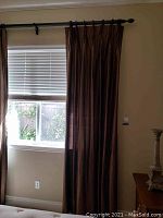 Silk drape hanging on black decorative curtain rod next to window with blinds.