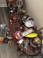 Overview of assorted metal items on wooden table including hat rack, lamp, decorative metal objects, plates, cups, and easels.