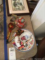 Photo showing a ginger jar, wooden painted spoons, porcelain plate, tiny painted porcelain items, fabric dolls, and framed wall art