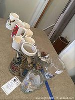 Overview of Orioles collectible mugs, beer steins, and pilsner glass on carpeted surface.