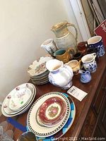 Overview photo of lot showing small pitchers, painted plates stacked, and painted bowls on a wooden surface