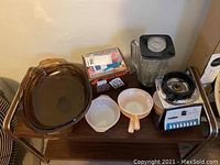 Lot of kitchen items including amber Fire King baking dishes, vintage Osterizer blender, boxed diet scale, and Corning Visions toaster.