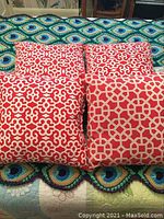 Four square pillows displayed on a colorful crocheted blanket, showing three identical red and white curly cue pattern pillows and one with octagon lattice pattern.