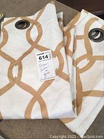 Pair of folded linen drapes with large cafe rings showing the gold circular pattern on ivory background