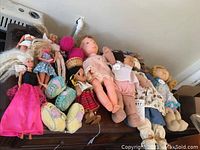 Overview of the mixed lot showing various dolls including Barbies, soft bodied dolls, and a large rag doll.