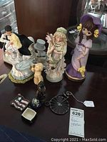 Wide view of mixed resin statues, including bride and groom, purple girl music box, lady figurine, dog, and small trinket boxes on table