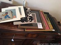 Stack of framed wall art featuring fabric and mixed media pieces on a wooden cabinet surface