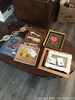 Photo of multiple framed artworks and empty frames on table, showing varying styles and subjects.