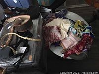 Lot of mixed fashion accessories showing scarves and purses stacked on a round table with belts on the side, some hats partially visible.