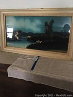 Full front view of one reverse glass painting showing landscape scene and cream wood frame