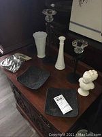 Two white milk glass vases, three black iron and glass candleholders, two heavy iron square plate candleholders, white lady bust, and curtain tie backs on wooden sideboard.
