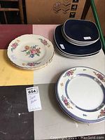 Photo showing 3 floral plates stacked and 7 square blue plates from Interior Collections.
