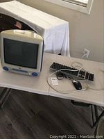 Full view of the Apple iMac G3 Blueberry desktop computer with keyboard, mouse, and power cord on a white table.