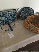 Side-by-side view of two Vera Bradley smaller purses in blue floral pattern, accompanied by a round wicker basket with handles on table.