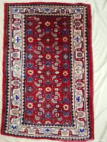 Full view of rectangular hand knotted Persian wool rug with floral and geometric patterns on a red field and ivory border.